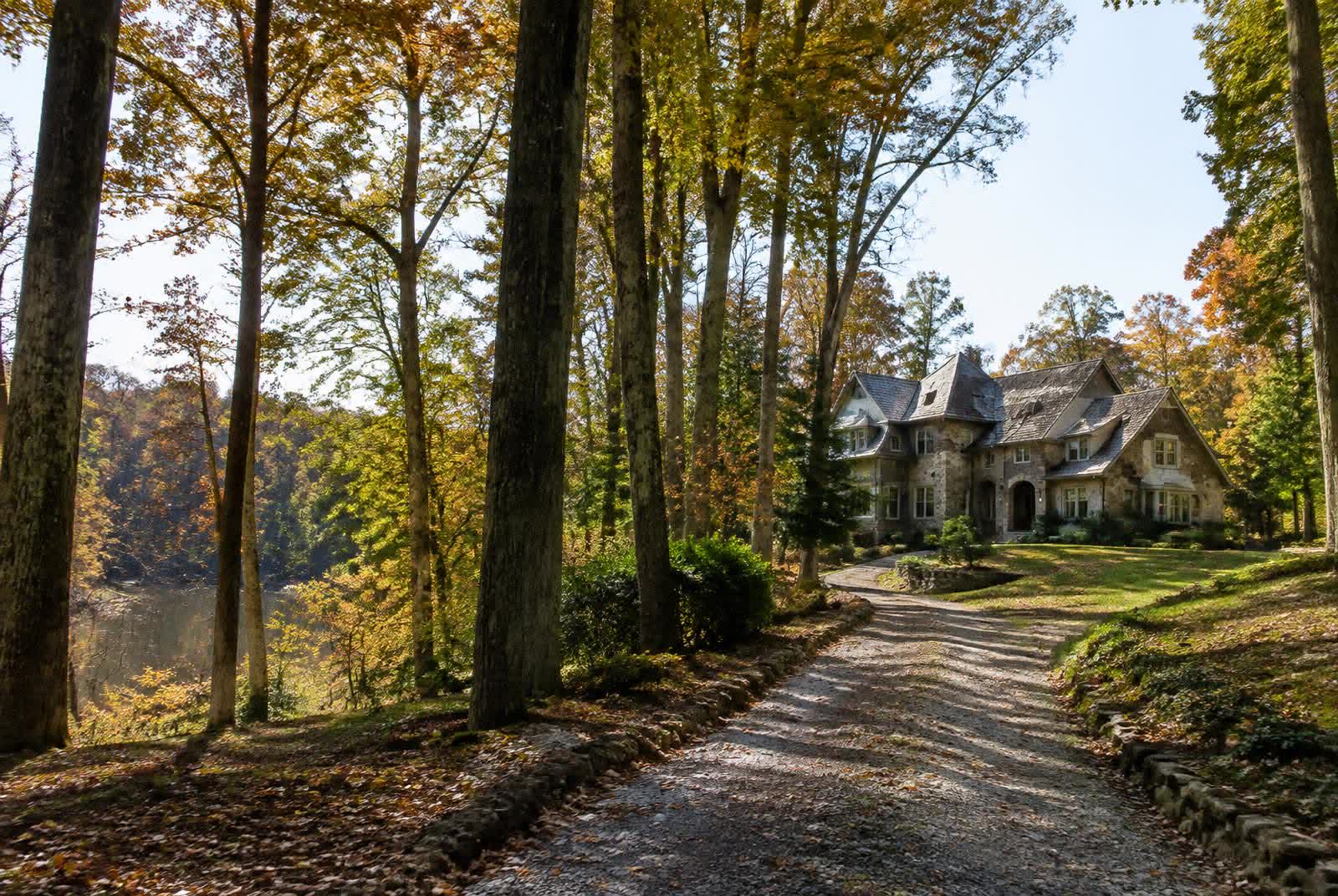 Stone estate home at the end of a gravel drive through mature hardwoods on a wooded acreage lot near Marvin, North Carolina