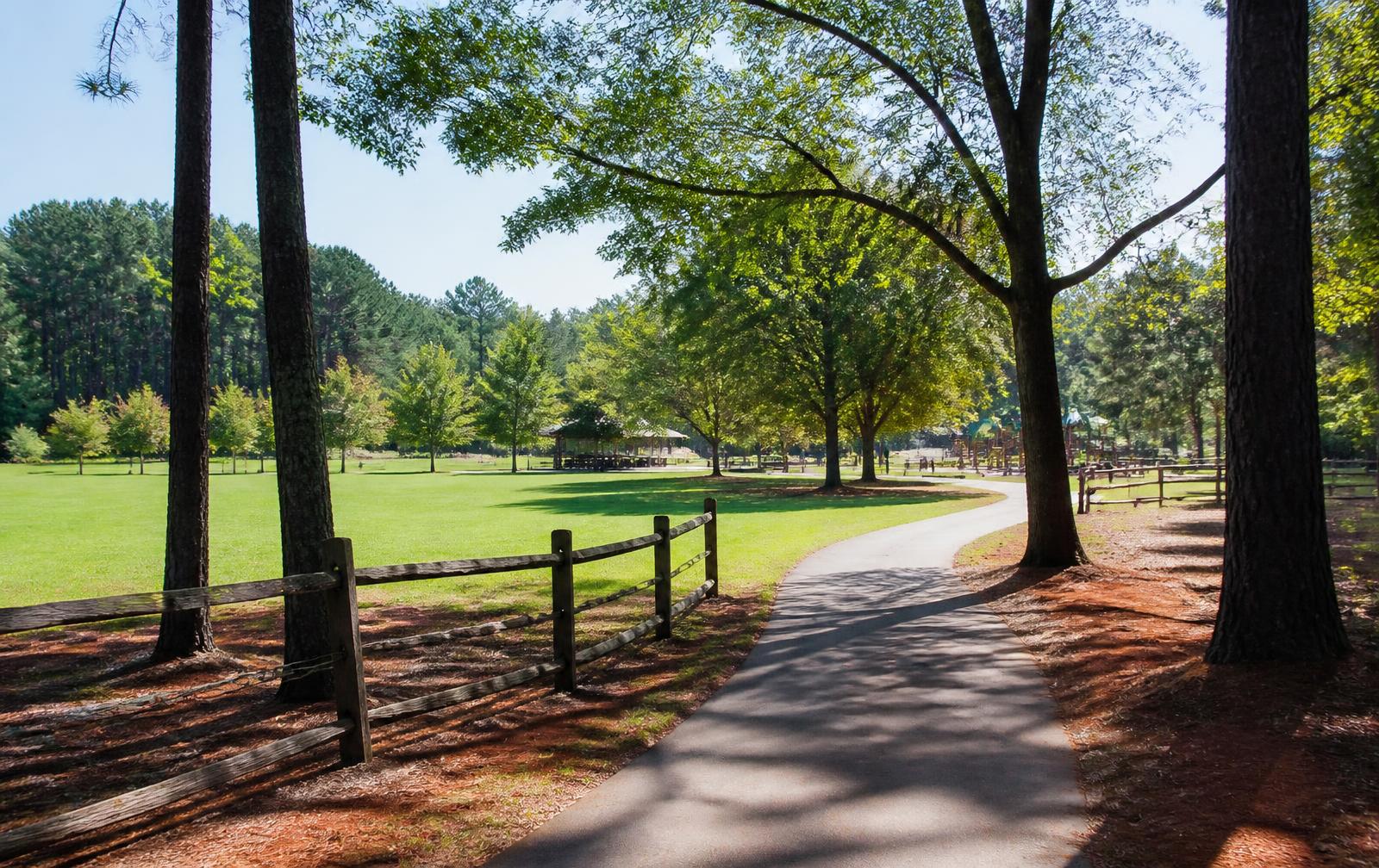 Paved greenway path curving through mature oaks and pines past a split-rail fence and open lawn at Marvin Efird Park in Marvin, North Carolina