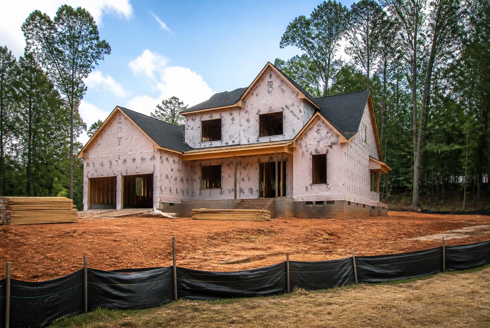 New construction home framed and wrapped on a graded lot with erosion control fencing near Marvin, North Carolina